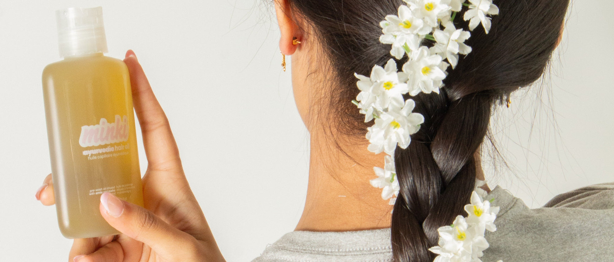 Person with a braid decorated with white flowers holding a bottle of Minki Hair Oil.