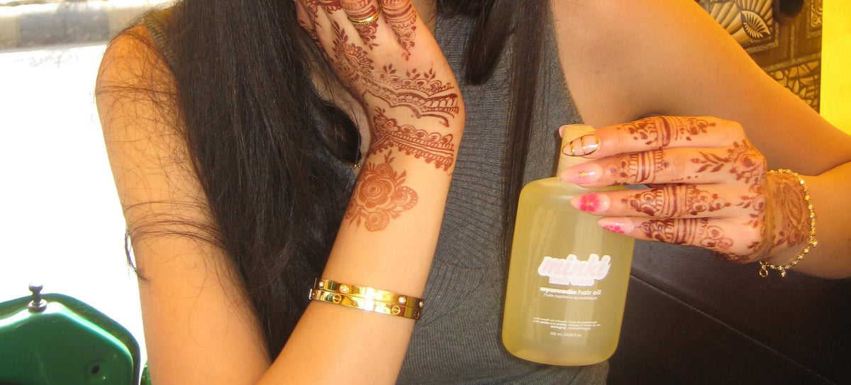 Woman with sunglasses and henna on her arm holding a bottle, with a yellow background